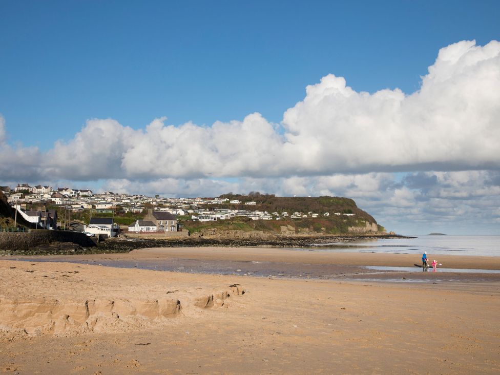 A beach with clouds and people walking at Big Azzles in Benllech