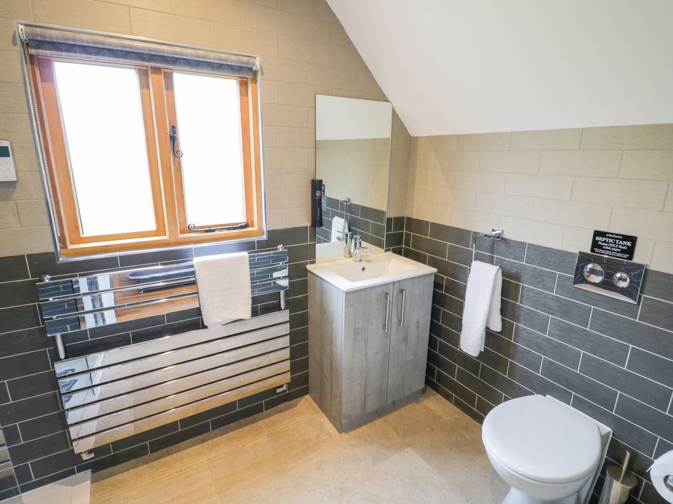 A bathroom with a sink, toilet, towel rail, and window at The Coach House in Chacombe