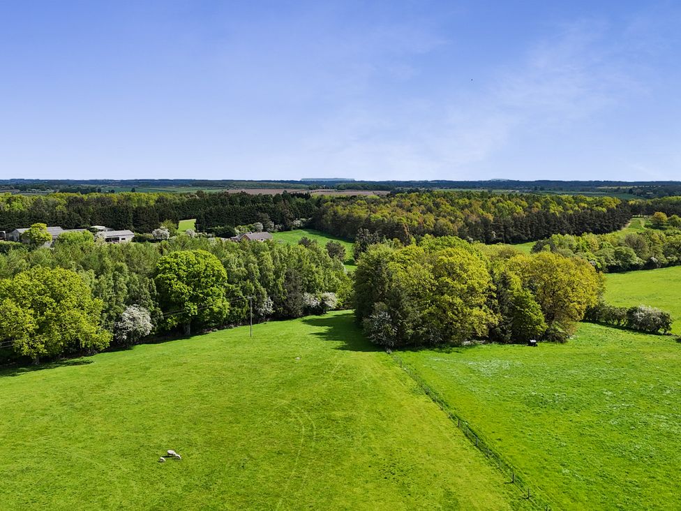 An aerial view of a green field with trees and buildings at Shepherd's Crook in Follifoot near Spofforth