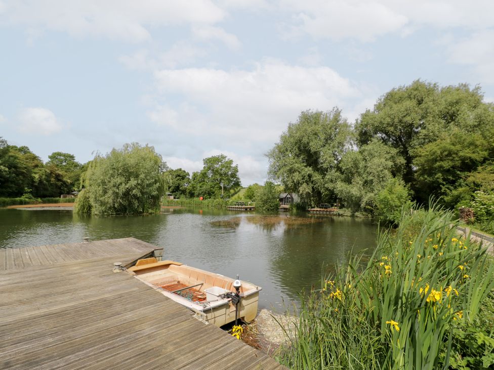 A pond with a boat and trees at Acorn Lodge At Bridge Lake Farm & Fishery Chacombe