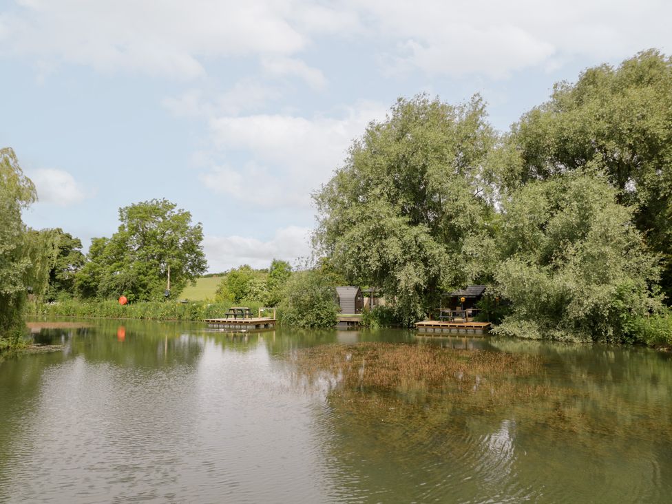 A pond with trees and dock at Acorn Lodge At Bridge Lake Farm & Fishery Chacombe