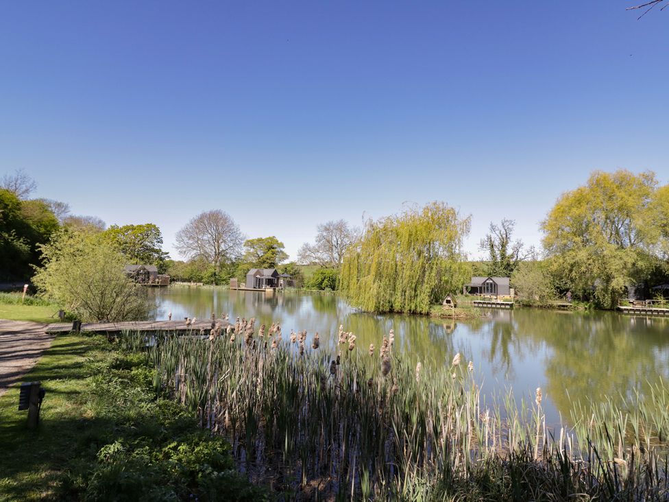 A scenic view of a lake with houses and greenery at Acorn Lodge At Bridge Lake Farm & Fishery Chacombe