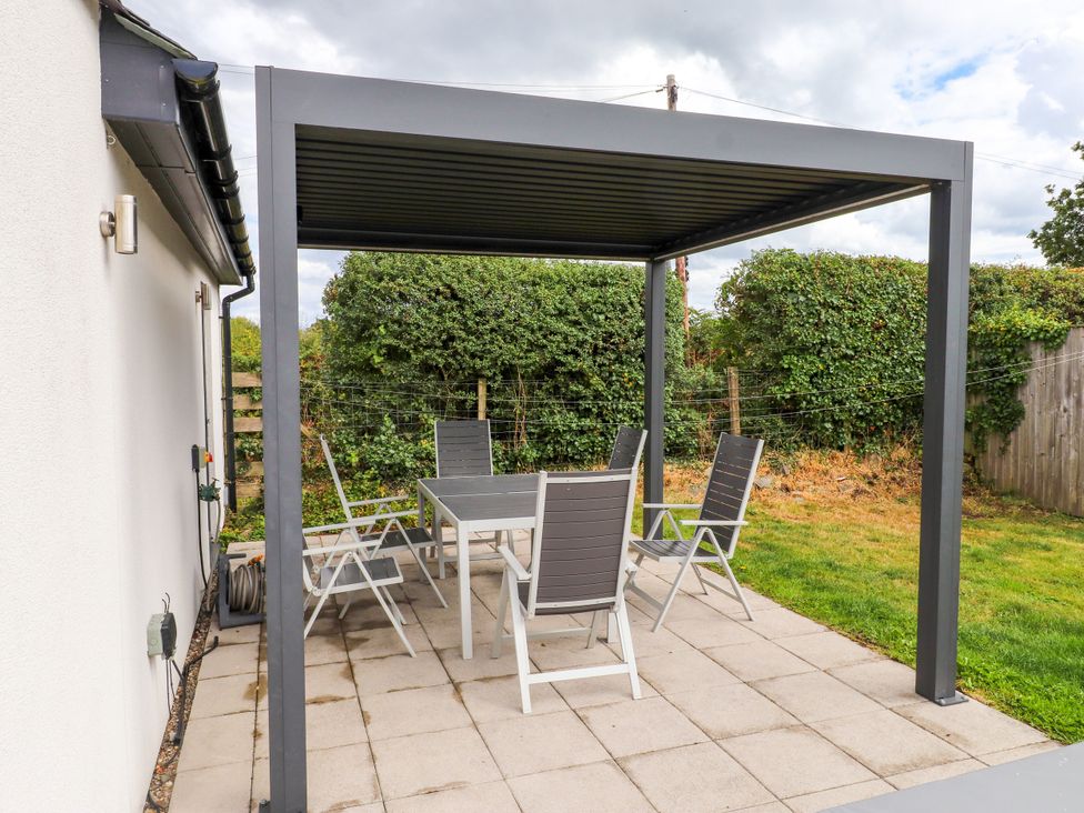 A patio with a table and chairs under a pergola at Pen Y Cefn