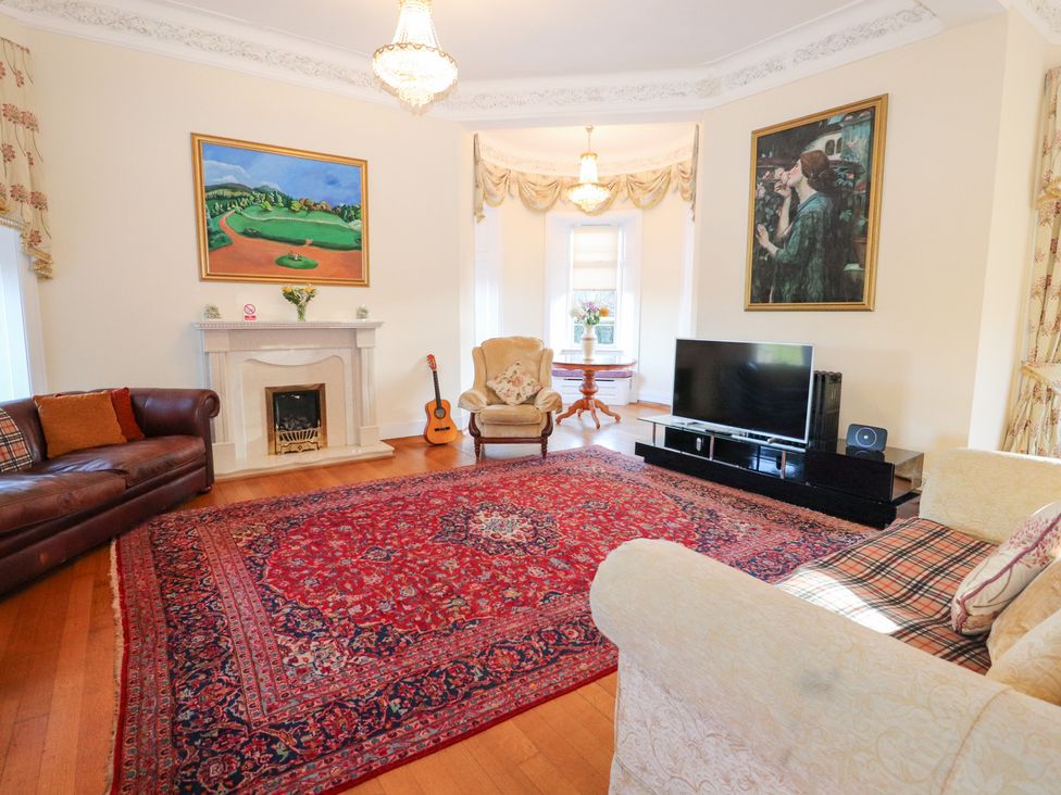 A living room with a sofa, armchair, coffee table, television, and fireplace at Auchentroig House in Buchlyvie