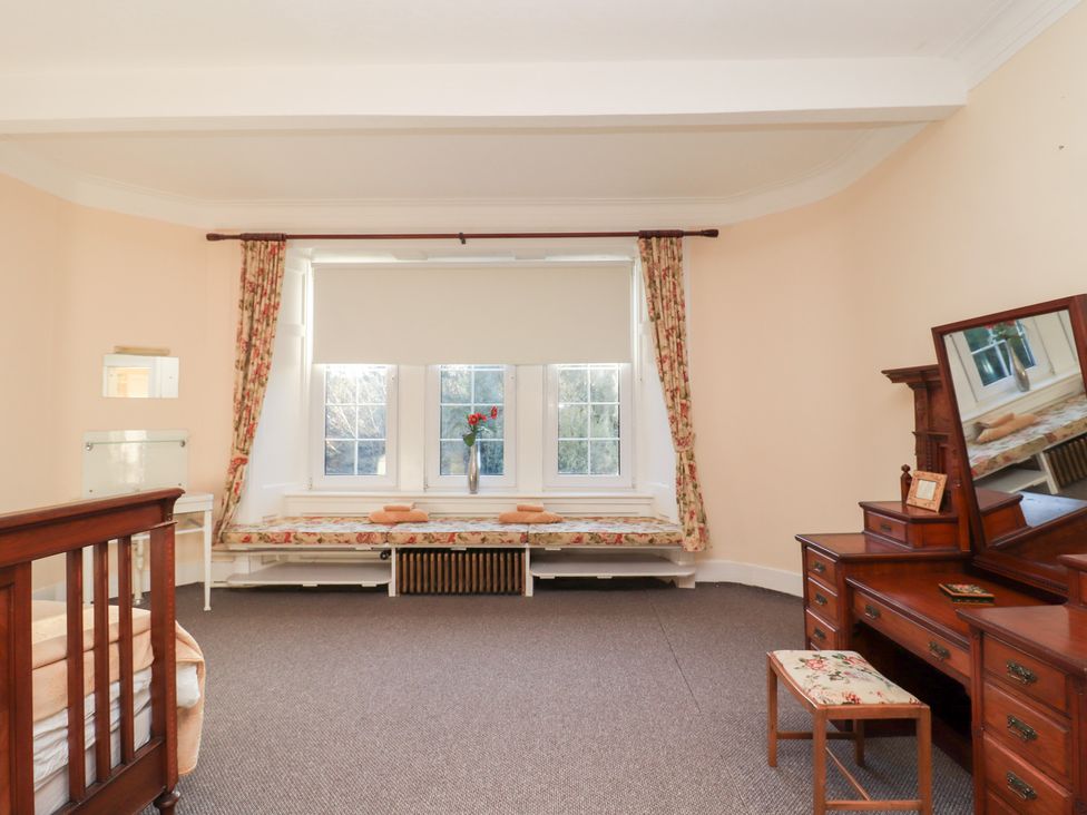 A bedroom with a bed, windows, and a dressing table at Auchentroig House in Buchlyvie