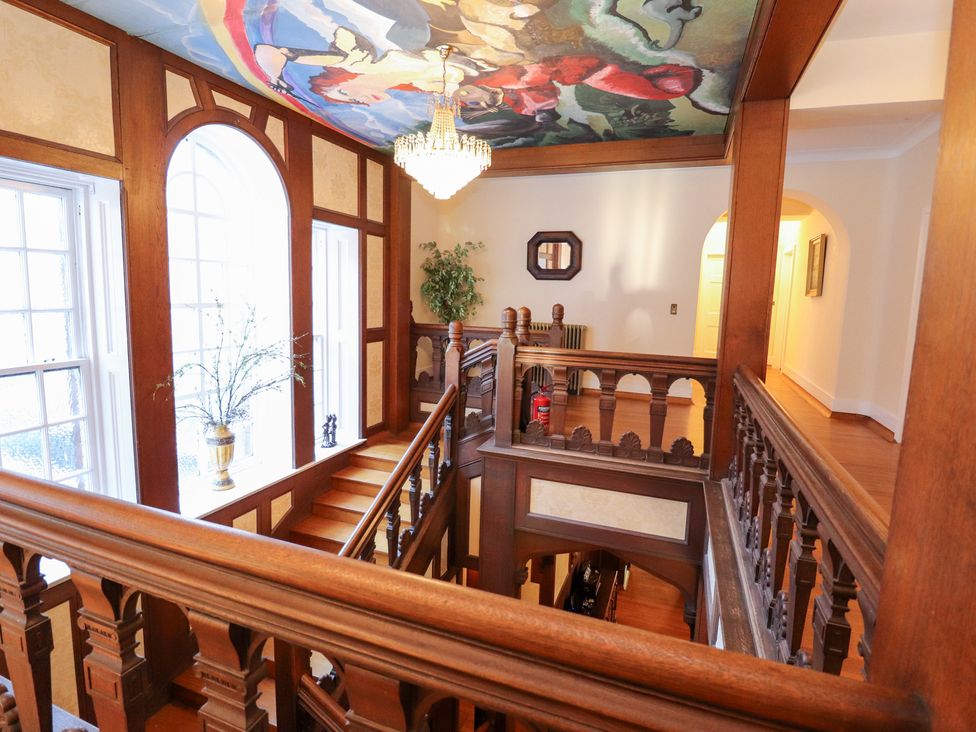 A hallway with stairs and a chandelier at Auchentroig House in Buchlyvie