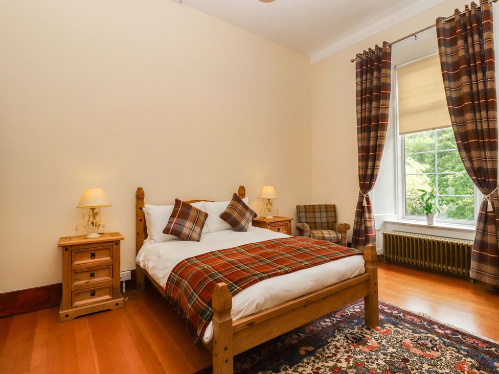 A bedroom with a bed, nightstand, chair, and window at Rob Roy Apartment Buchlyvie