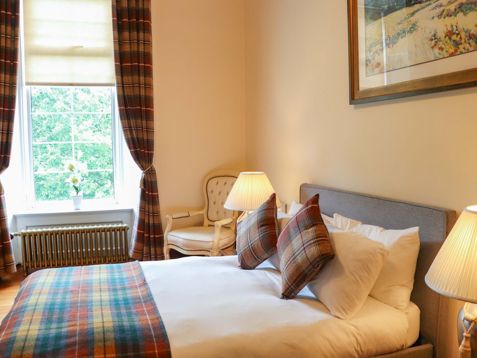 A bedroom with a bed and an armchair at Rob Roy Apartment in Buchlyvie