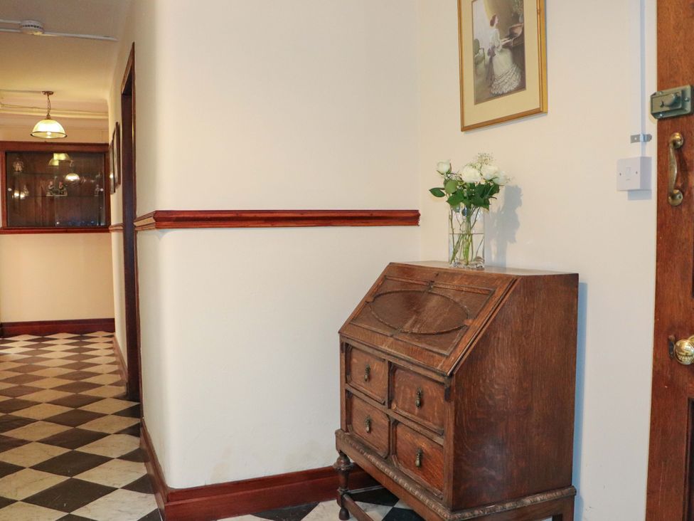 A hallway with a wood cabinet and a vase of flowers at Rob Roy Apartment in Buchlyvie