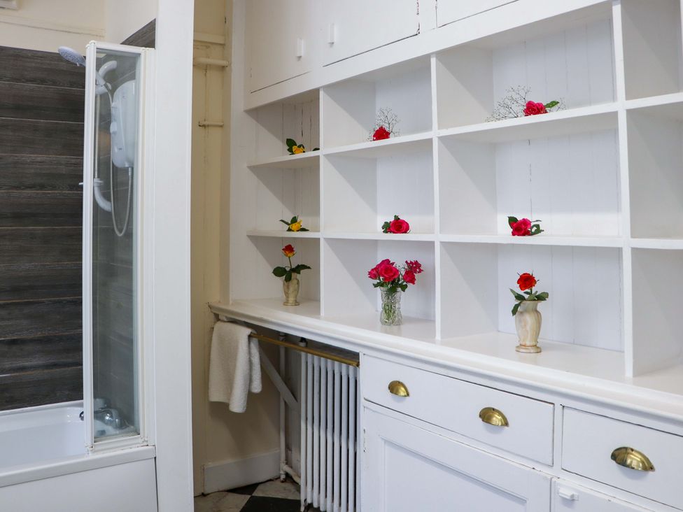A bathroom with a shower and shelf displaying flowers at Rob Roy Apartment in Buchlyvie