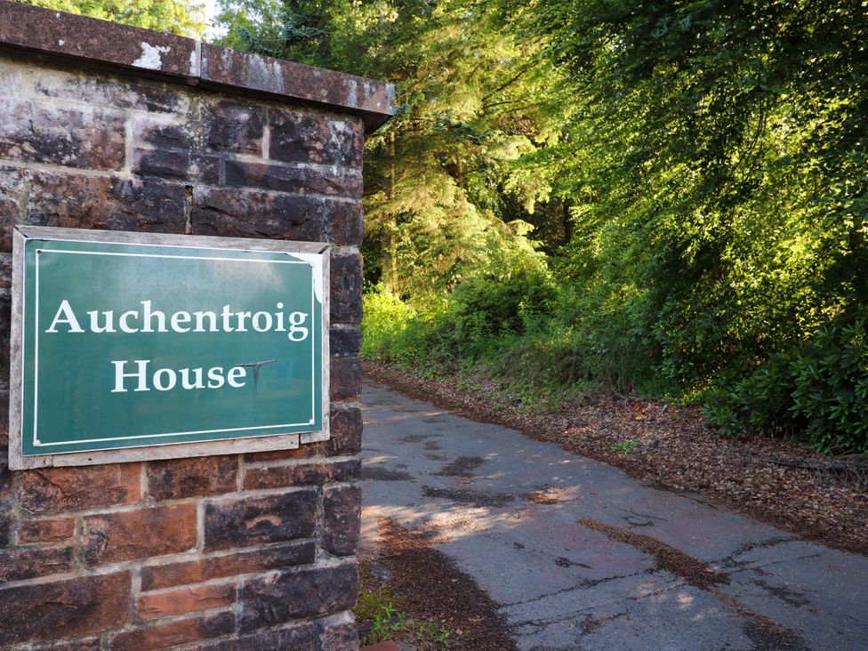A sign for Auchentroig House with trees and a pathway in the background