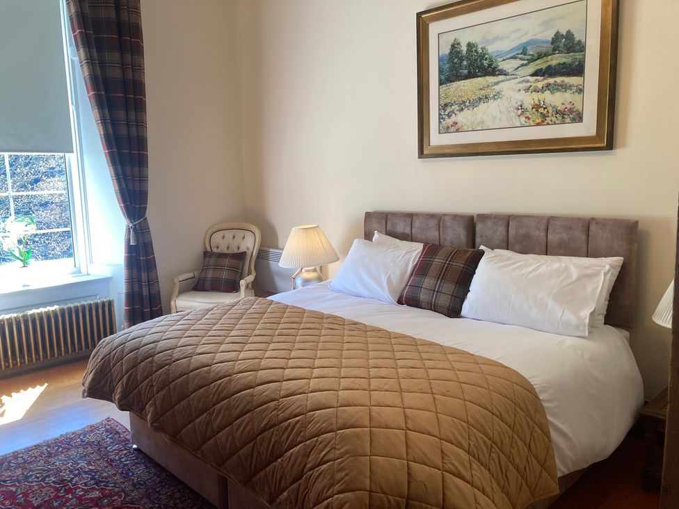 A bedroom with a bed, chair, and window at Rob Roy Apartment in Buchlyvie
