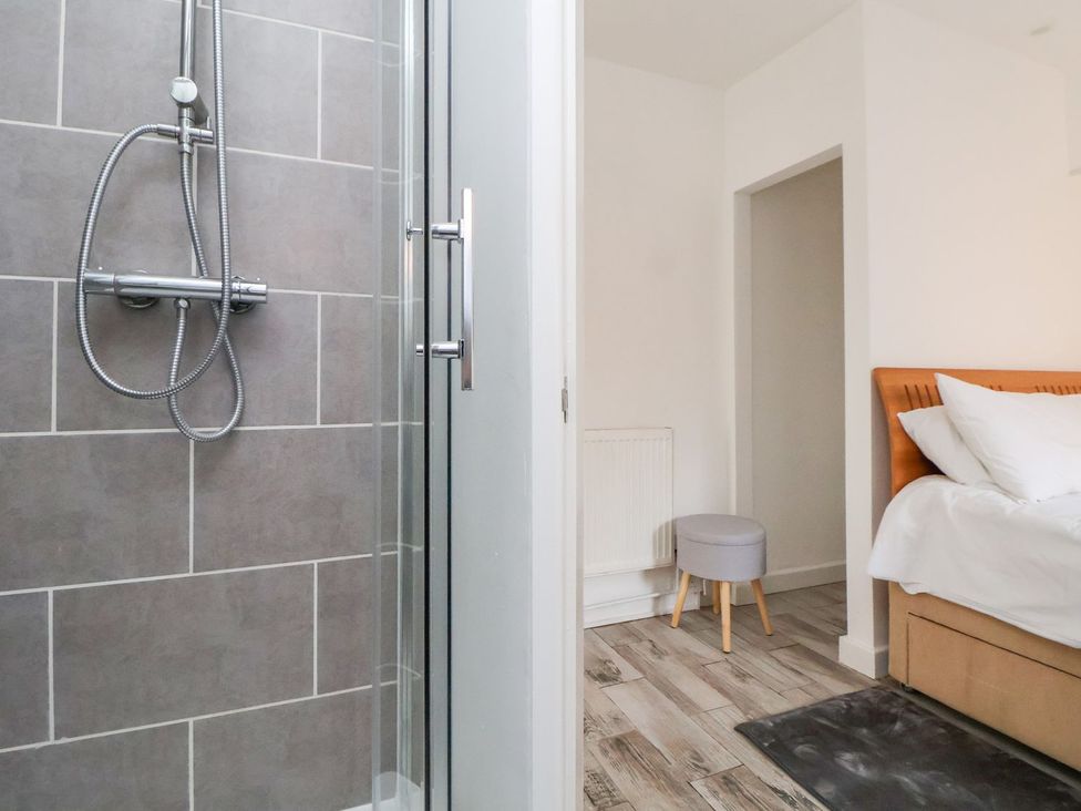 A shower area with a glass door and a bed in an adjoining room at Castellolwg