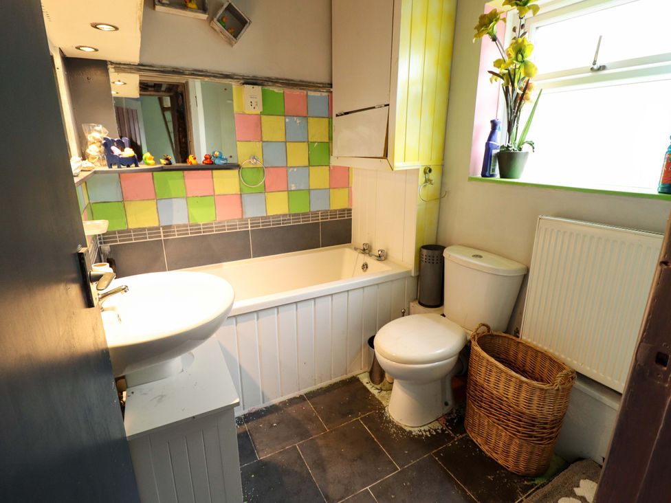 A bathroom with a bathtub, sink, toilet, and mirror at Dormy Cottage in Skegness