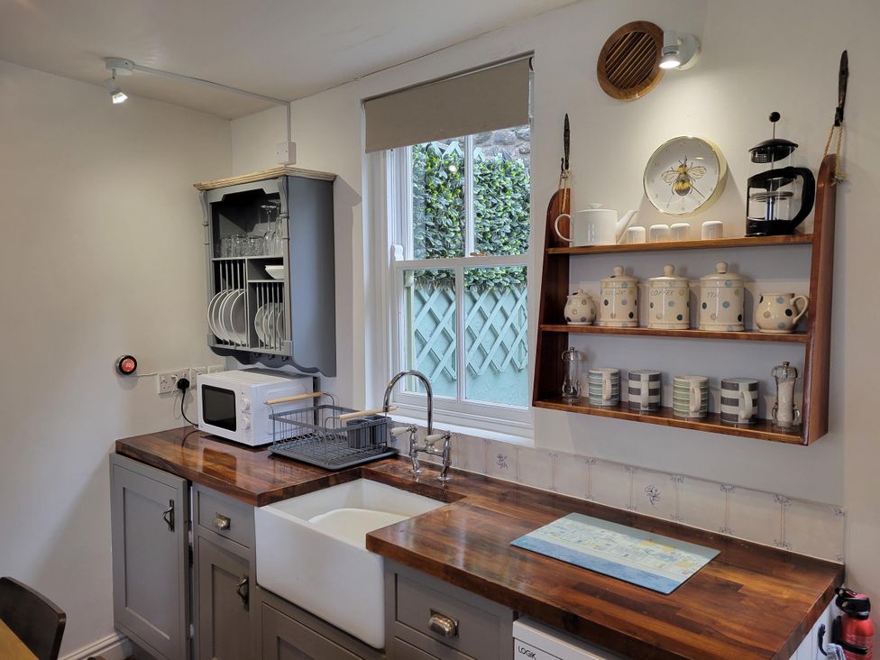 A kitchen with sink and shelf holding dishes at Millgate Cottage in Conwy