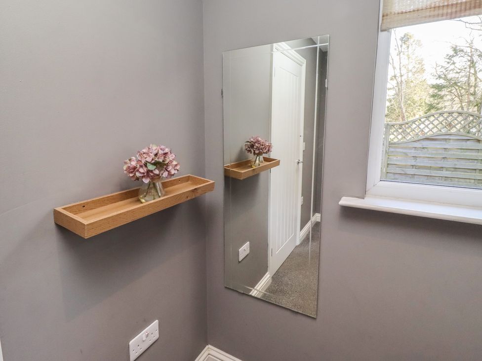 A hallway with a mirror and shelf containing flowers at Barn Owl in Otterburn