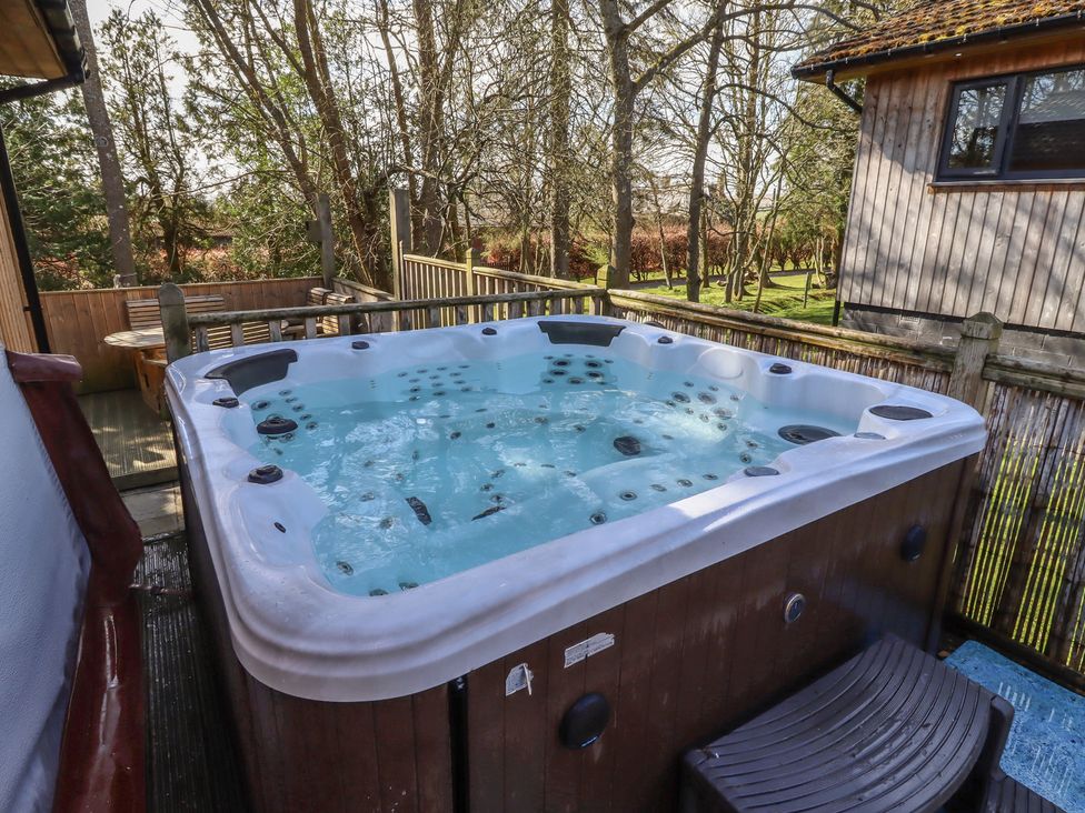 A hot tub on a deck surrounded by trees at Barn Owl in Otterburn