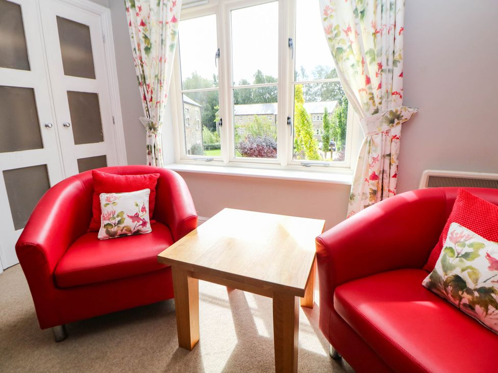 A living room with red armchairs and a wooden table at Hassop in Matlock