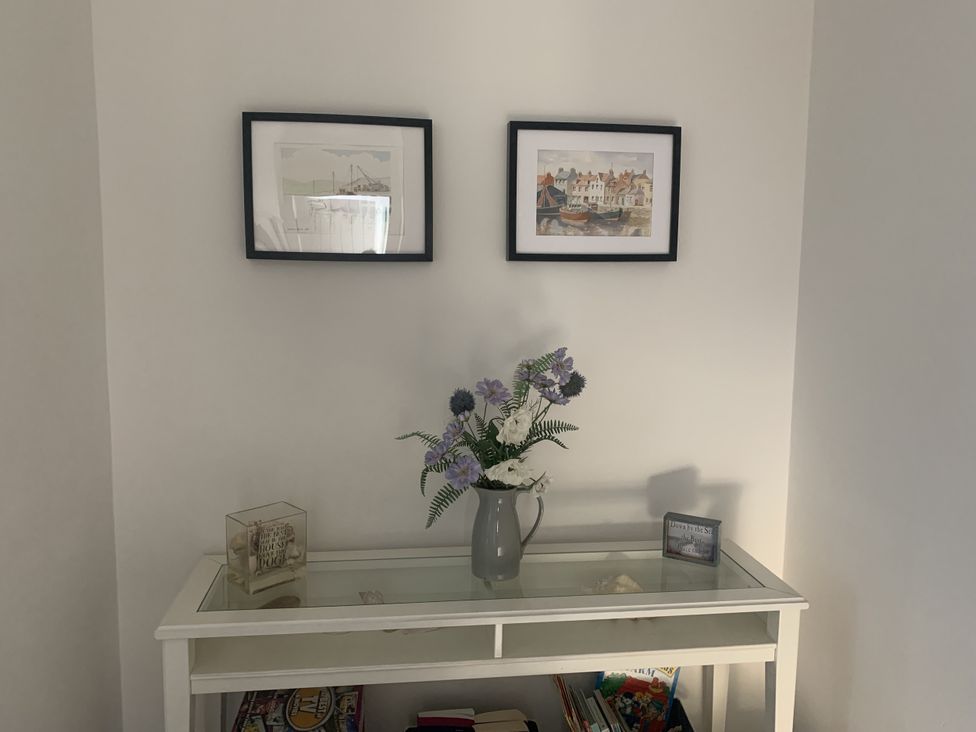 An entryway with photographs on the wall and a table with a vase and books at The Nest in Beadnell