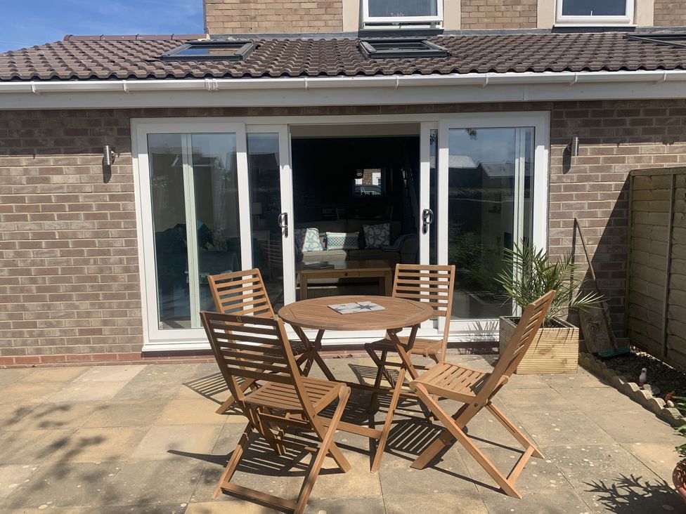 A garden with a table and chairs in front of sliding doors at The Nest in Beadnell