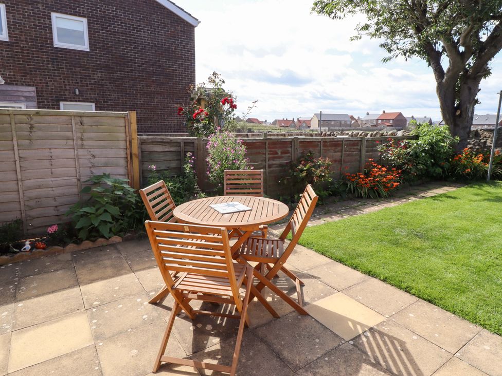 A garden with a wooden table and chairs at The Nest in Beadnell