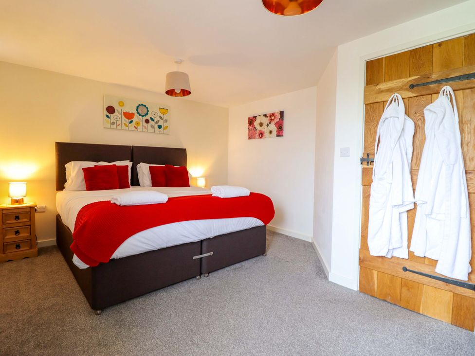 A bedroom featuring a bed with red accents, a side table, and decorative paintings at Bwthyn Y Bugail (Shepherd's Cottage) Pedairffordd near Llanrhaeadr-Ym-Mochnant