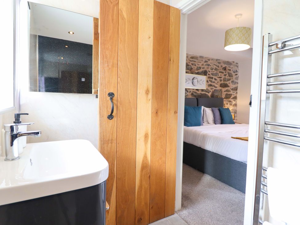 A bathroom with a sink and a wooden door leading to a bedroom at Bwthyn Y Bugail (Shepherd's Cottage) Pedairffordd near Llanrhaeadr-Ym-Mochnant