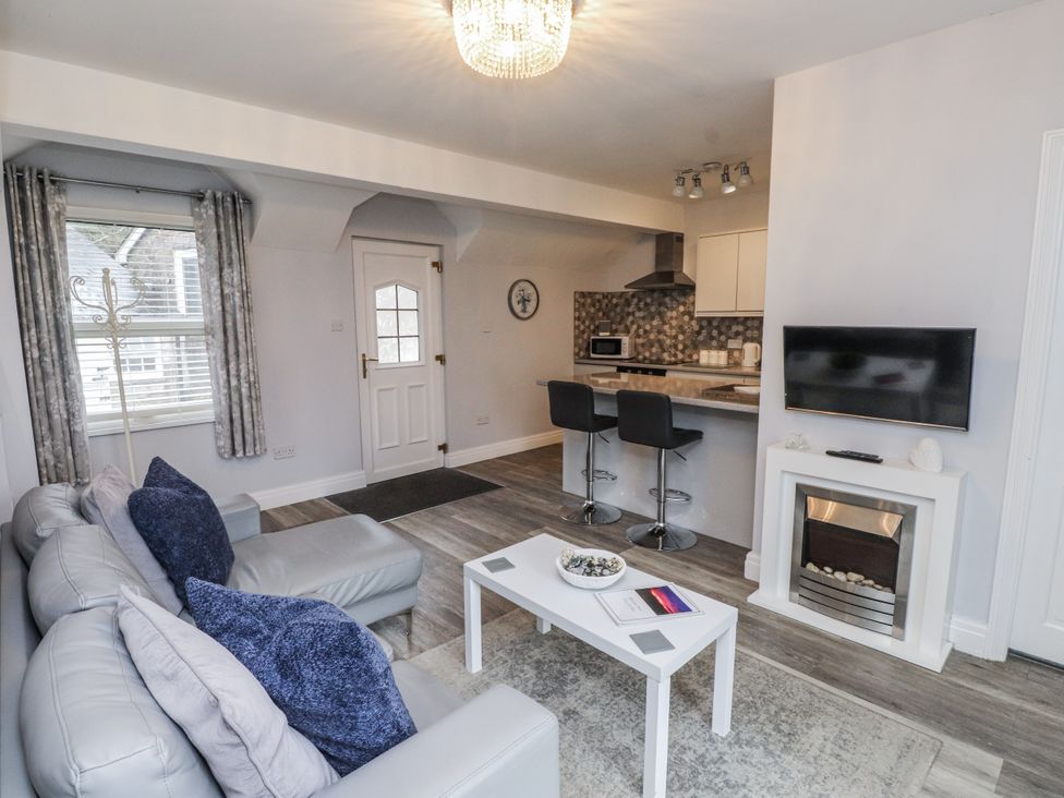A living room with a sofa, coffee table, and kitchen area at The Wren in Llysfaen