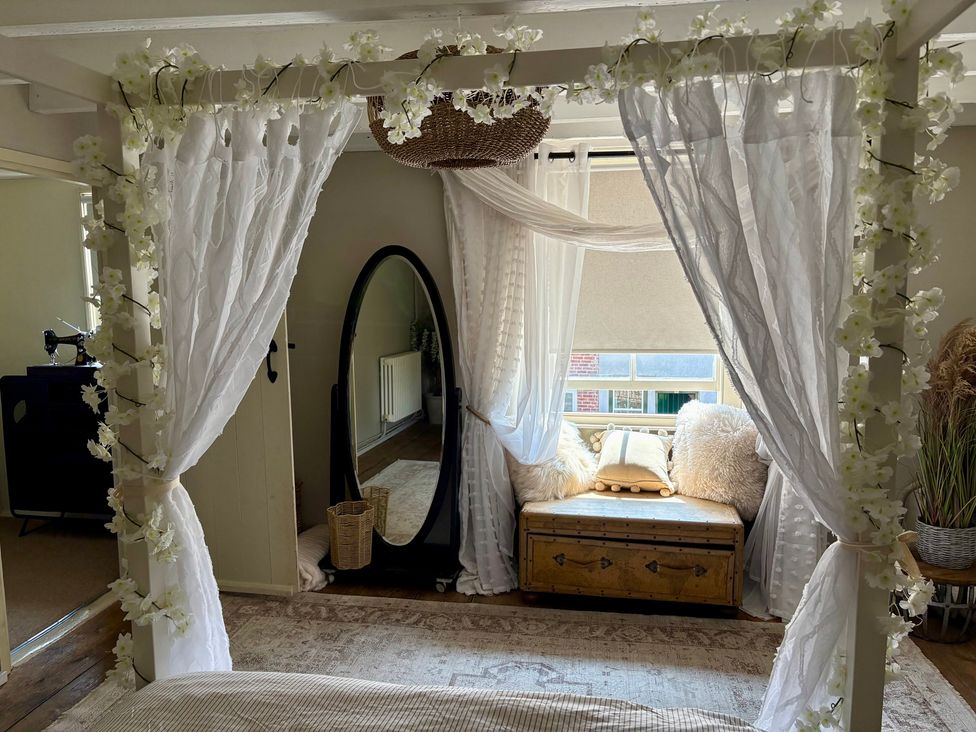 A bedroom with a bed, mirror, and settee at Coupling Cottage in Belper