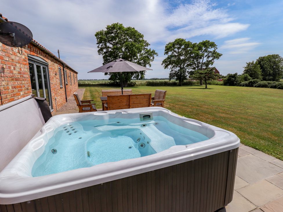 A hot tub with a table and chairs under an umbrella at The Stables in Wrangle near Old Leake