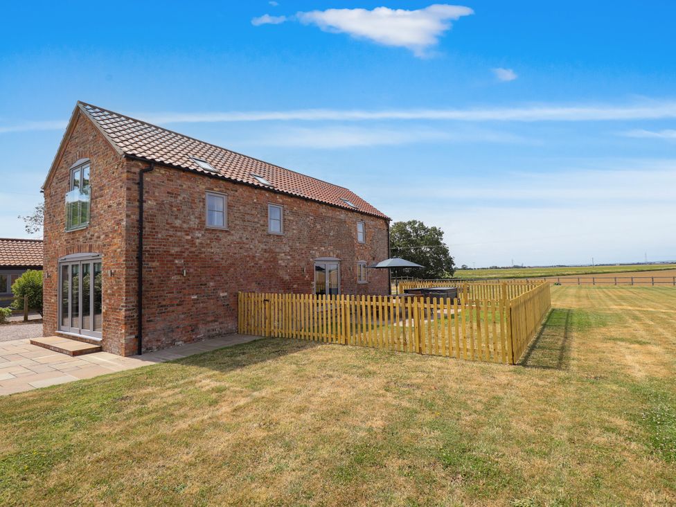 A brick house with a fence and patio in the garden at Acacia Barn Wrangle near Friskney