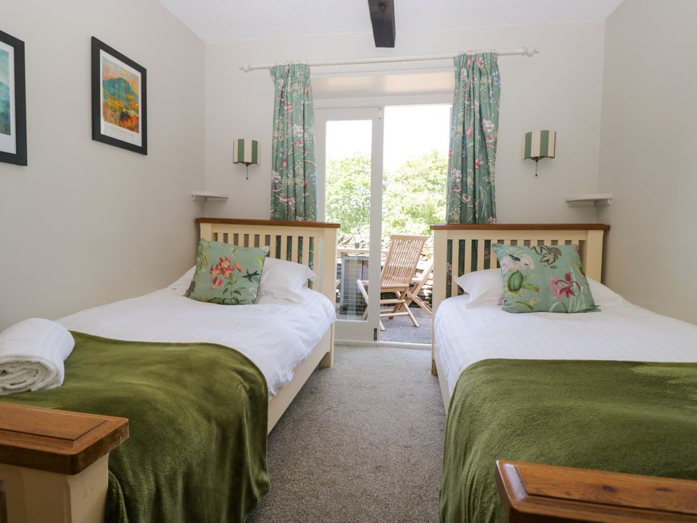 A bedroom with two beds and a door leading to an outdoor area at Windermere at the Graythwaite Estate near Hawkshead