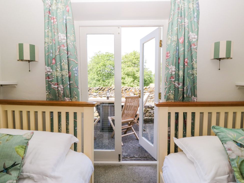 A bedroom with two beds and open doors leading to a patio area at Windermere at the Graythwaite Estate near Hawkshead