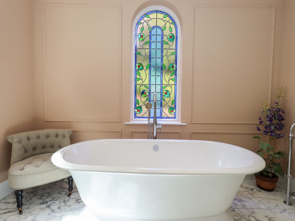 A bathroom with a bathtub and a stained glass window at High Torver House in Torver