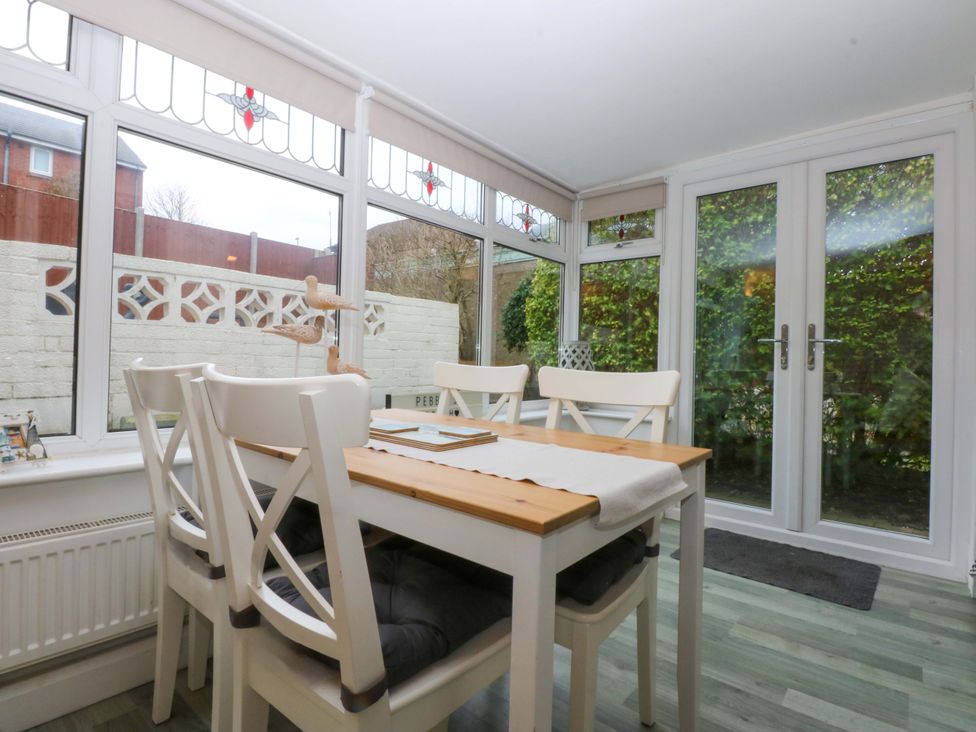 A conservatory with a dining table and chairs at Pebbles Reach in Colwyn Bay