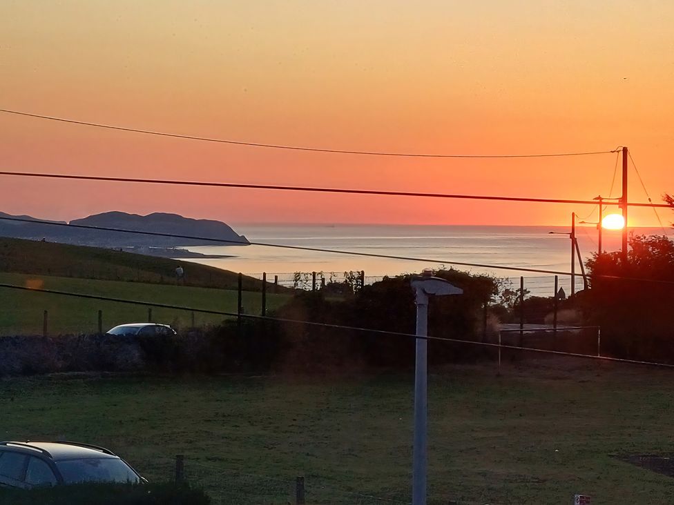 A sunset over the ocean with hills and power lines at Pebbles Reach in Llysfaen