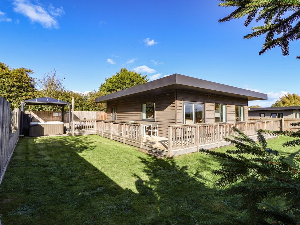 A log cabin with a deck and hot tub in the garden at Bluebell Wood in Brandesburton