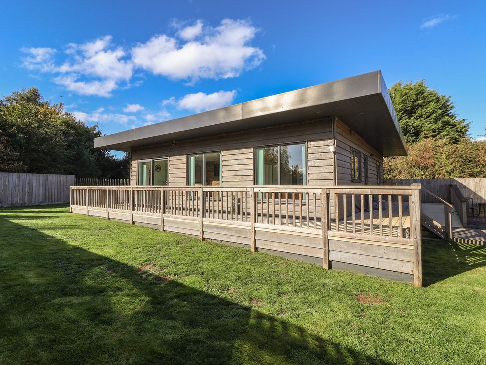 A wooden building with a deck and grass area at Bluebell Wood in Brandesburton