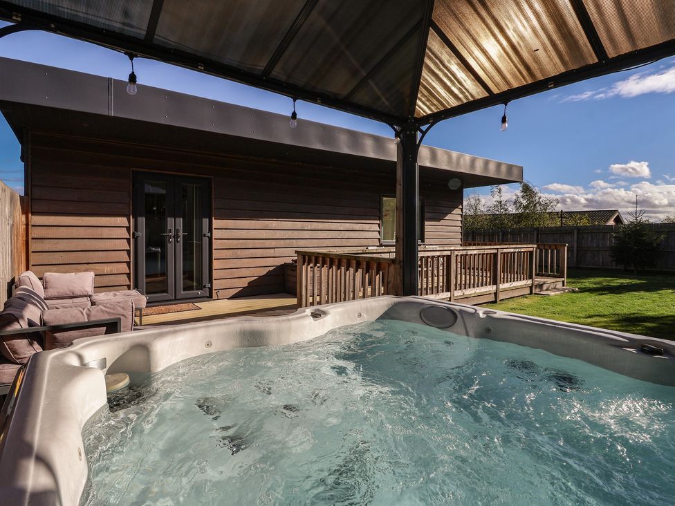A hot tub near a wooden deck and couch at Bluebell Wood in Brandesburton