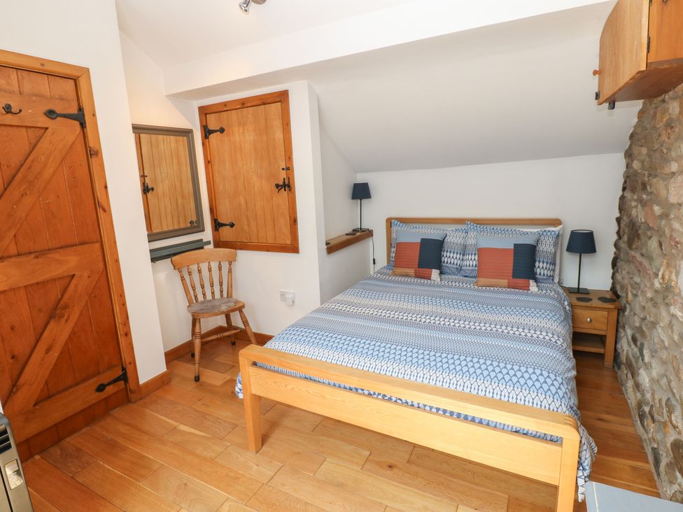 A bedroom with a bed, chair, and mirror at Chapel Cottage in Sandford, Cumbria