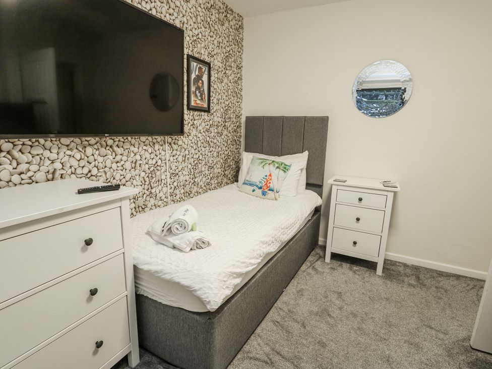 A bedroom with a bed, TV, dresser, and mirror at Daisy Cottage in Benllech