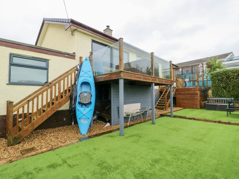 A garden with a kayak on the side and stairs leading to a deck at Daisy Cottage Benllech