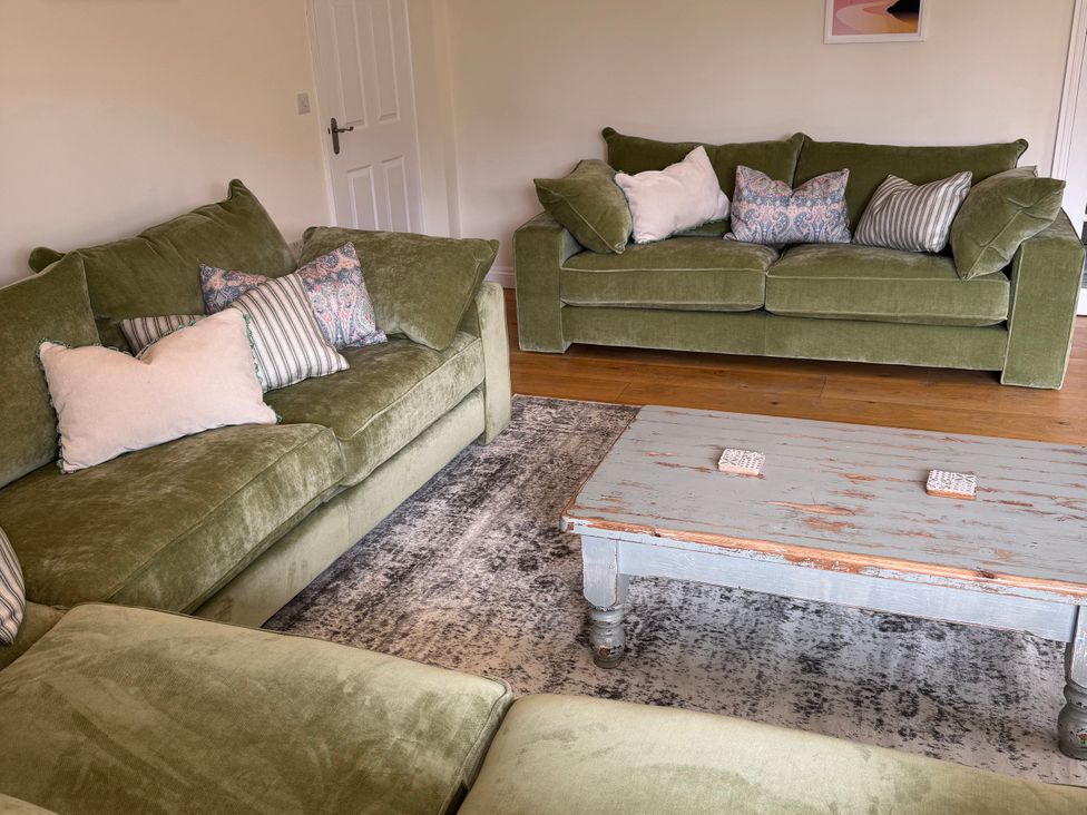 A living room with green sofas and a coffee table at Trevose House in Crantock