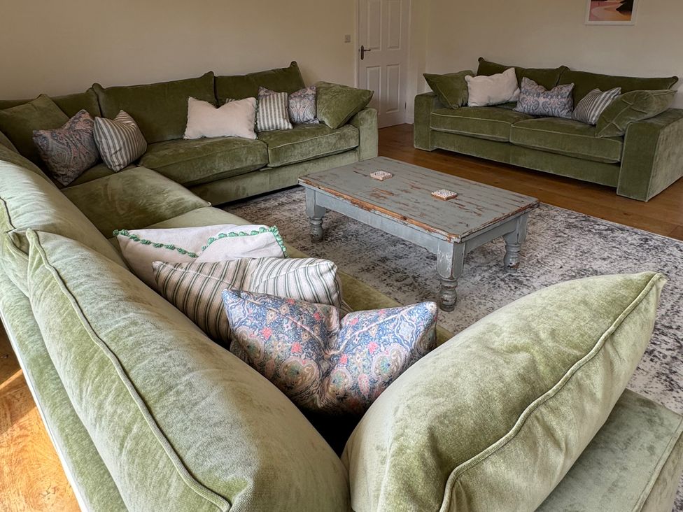 A living room with green sofas and a wooden coffee table at Trevose House in Crantock