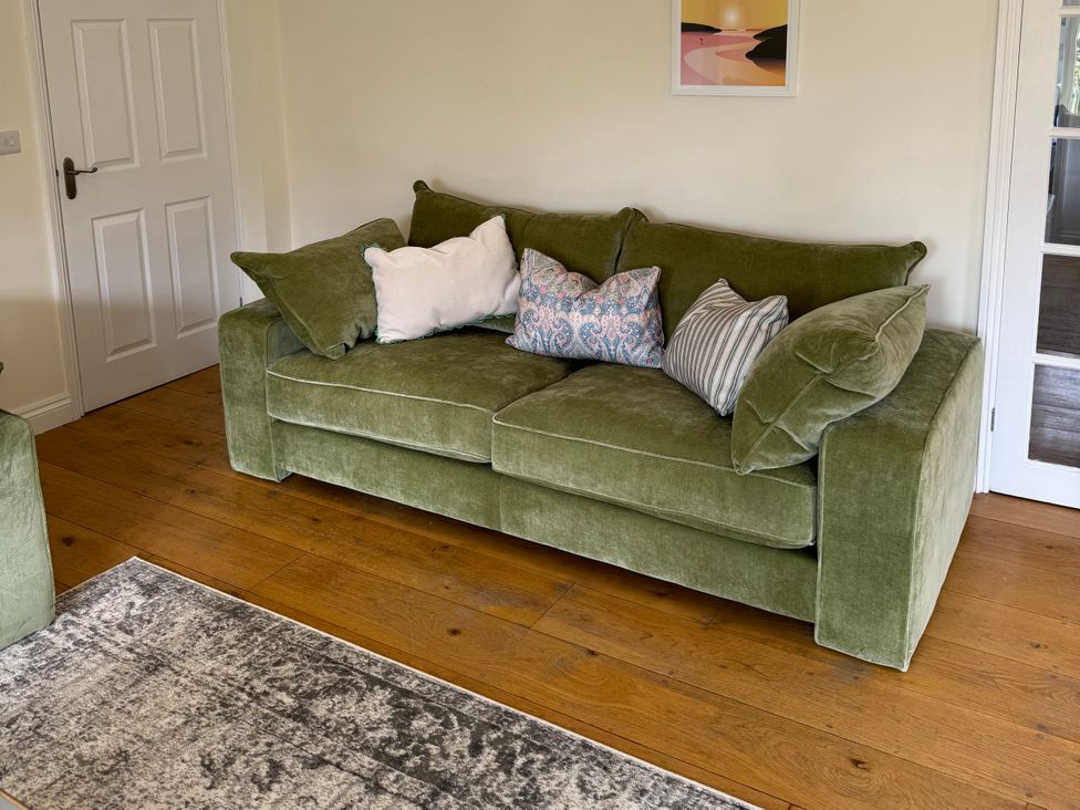 A living room with a green sofa and cushions at Trevose House in Crantock