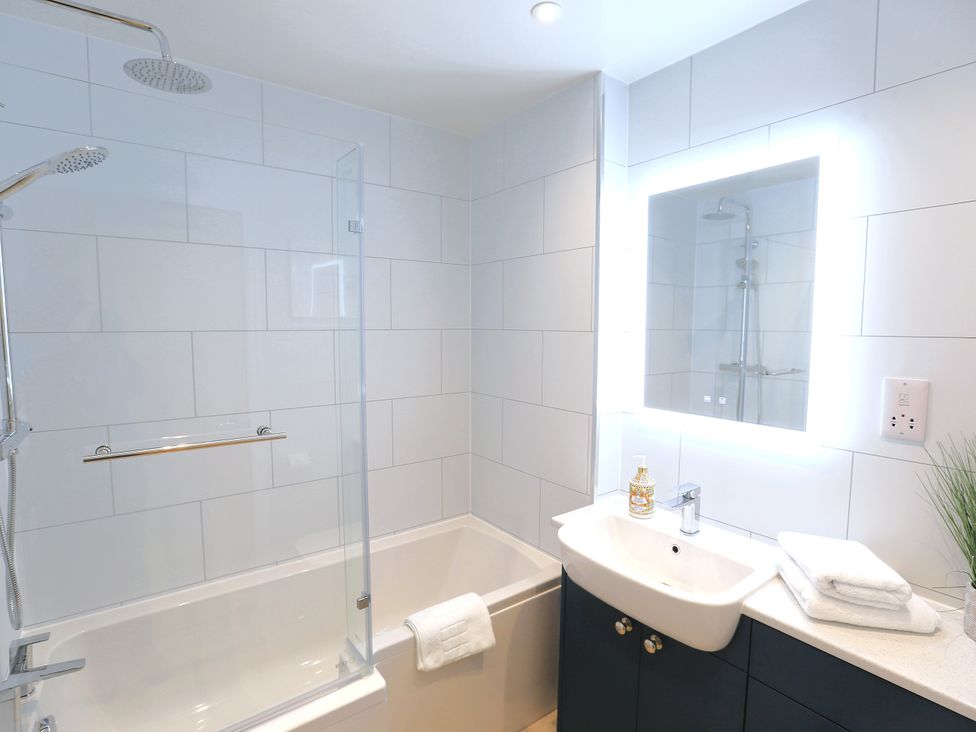 A bathroom with a bathtub, shower, and sink at Honeybee Cottage in Penruddock