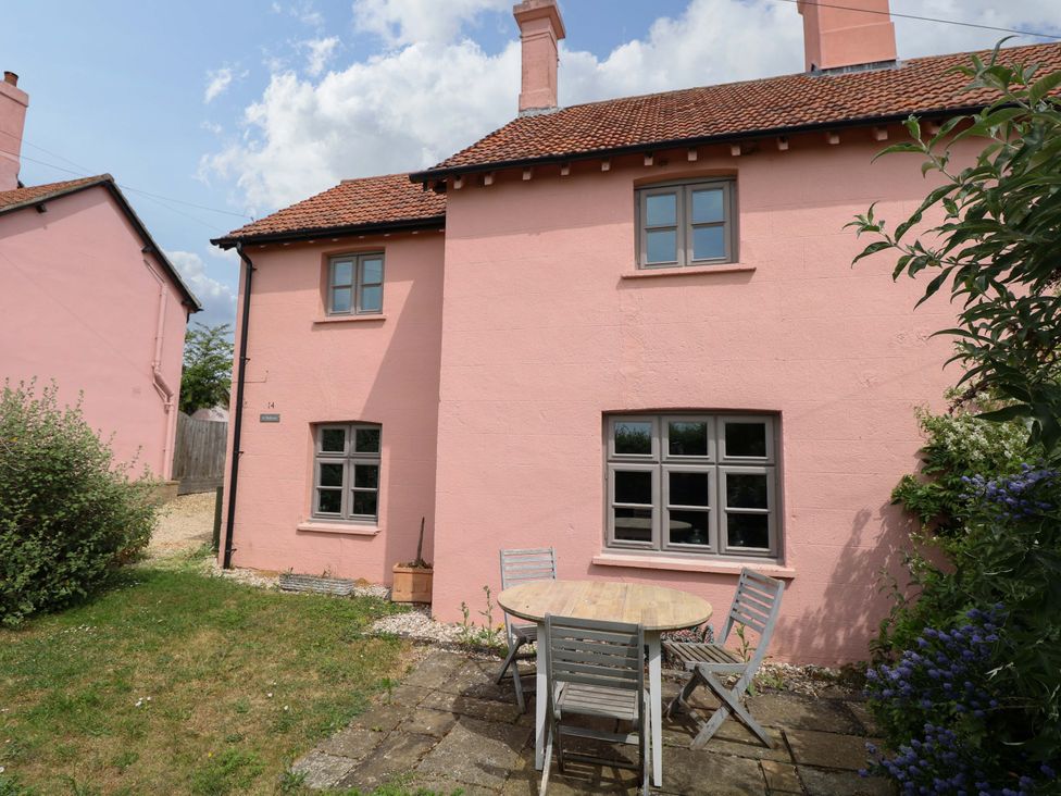 A pink house exterior with a table and chairs in the garden at The Mallows in Walsingham
