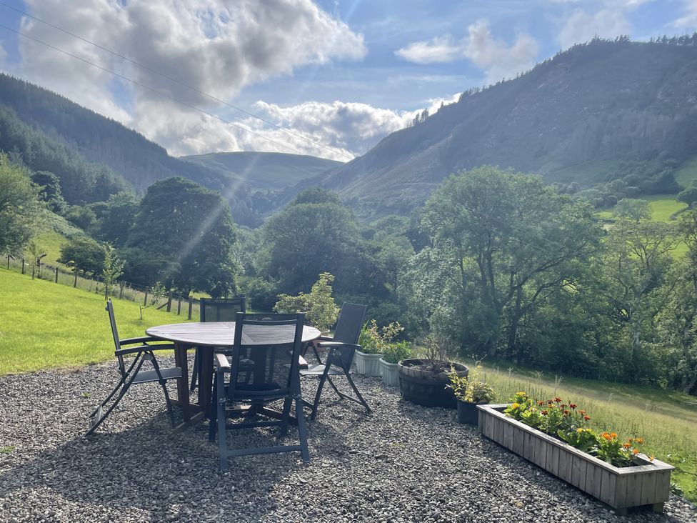 A table and chairs on a patio with a view of mountains at Graig Las The Barn located in Llangynog near Llanrhaeadr-Ym-Mochnant