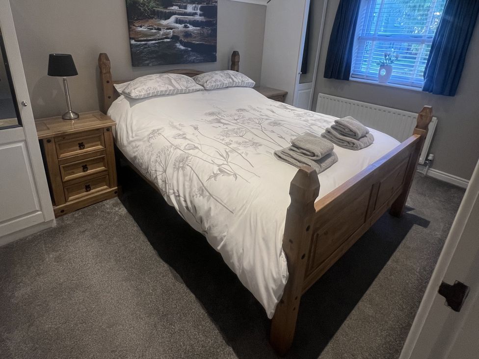 A bedroom with a wooden bed and bedside table at Honeysuckle Cottage in Richmond