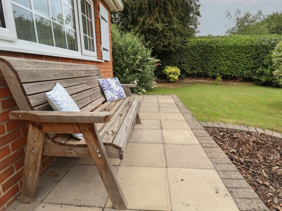 A garden with a wooden bench and cushions at Marsh View Cottage in Wainfleet All Saints